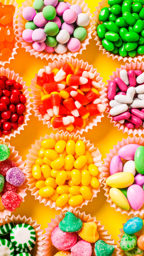 Multicoloured candy and jellybeans in paper cups overhead screenshot