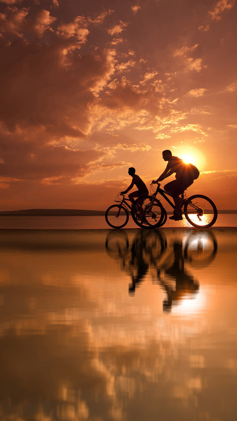 Two mountain biker silhouettes at sunrise on water screenshot