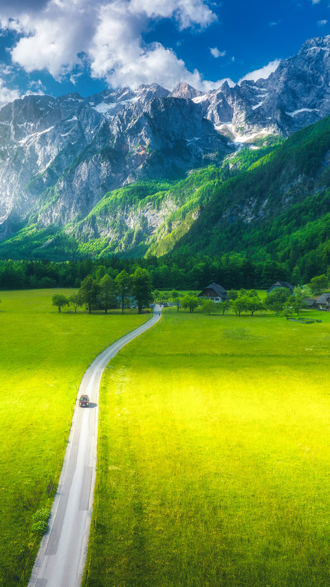 View of road, alpine mountains,, trees in summer at sunset screenshot