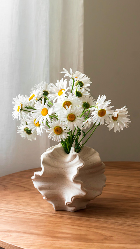 A bouquet of daisies in a ceramic vase on a wooden table screenshot