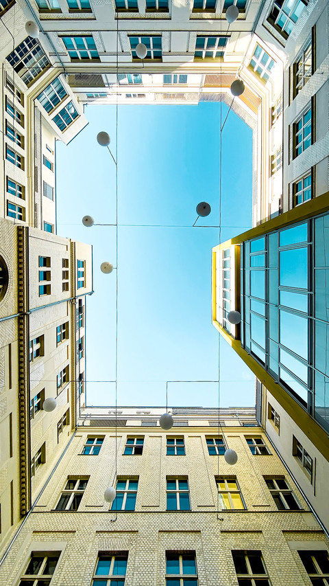 Low angle view courtyard of apartment block against blue sky screenshot