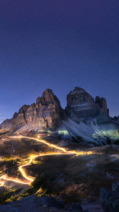 Car light trails on mountain road and high rocks at night screenshot