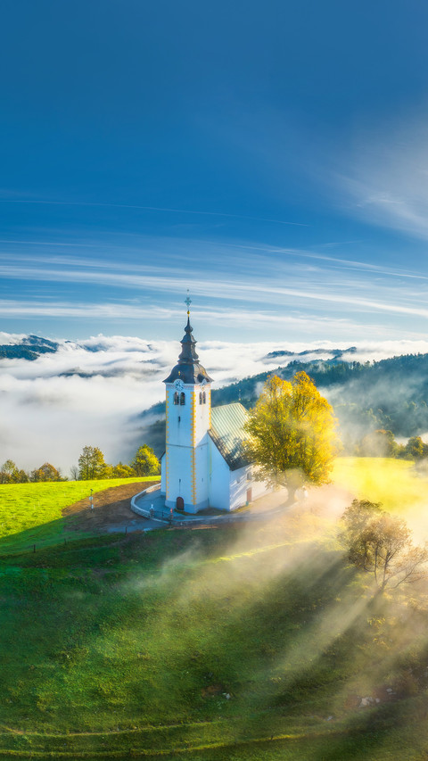View of small church on the hill in low clouds at sunrise screenshot