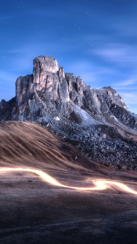 Car light trails on mountain road and high rocks at night screenshot