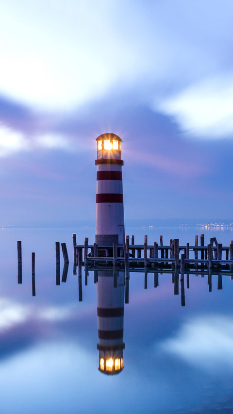 A lighthouse reflected in a lake during colorful sunset screenshot