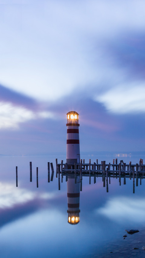 A lighthouse reflected in a lake during colorful sunset screenshot