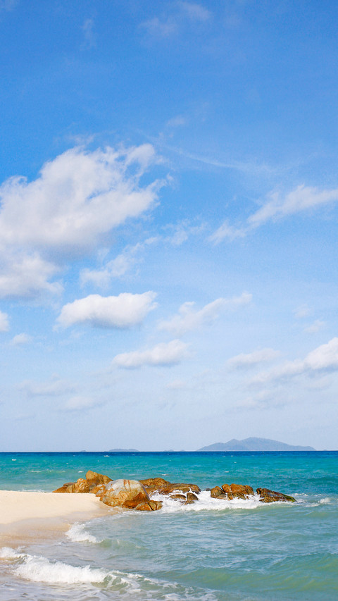 Clean beach and stones extending into body of blue sea screenshot