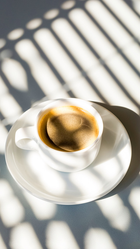 White cup of coffee in sunlight and shadows from above screenshot