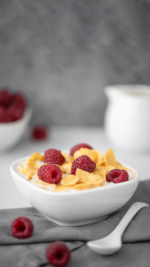 Cornflakes with milk and raspberries on a white table screenshot